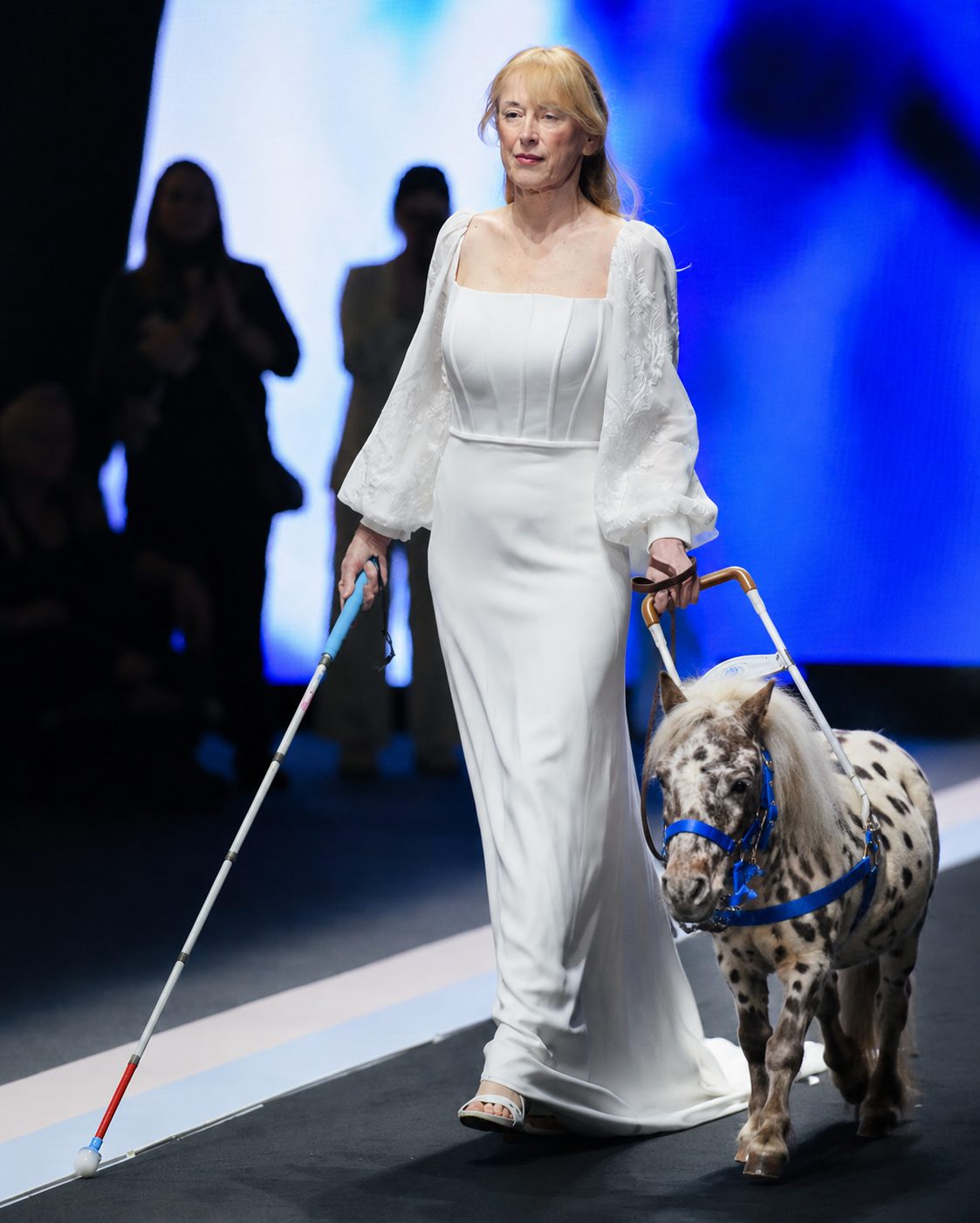 Modella in abito bianco guidata da un mini pony maculato